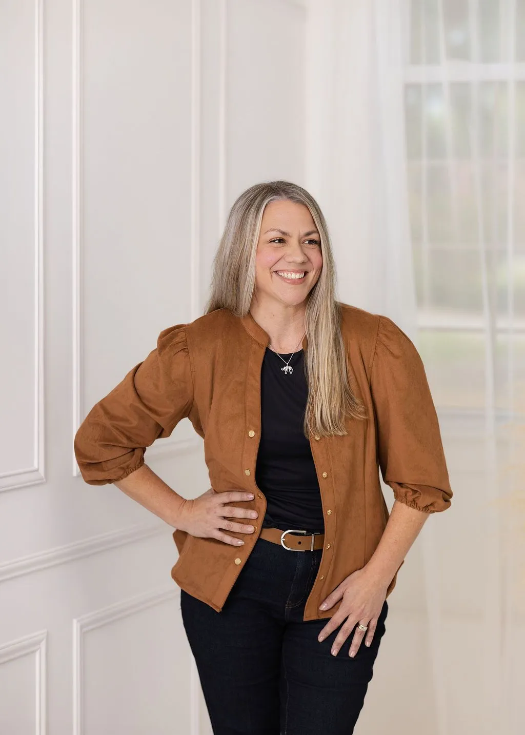 Alexis Goines standing and smiling in a warm brown jacket
